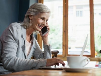 pikwizard smiling senior woman talking on mobile phone while working on laptop center top